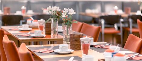 Un comedor con mesas dispuestas para el servicio, con jarrones de vidrio transparente con flores y una cesta de mimbre en una de las mesas.