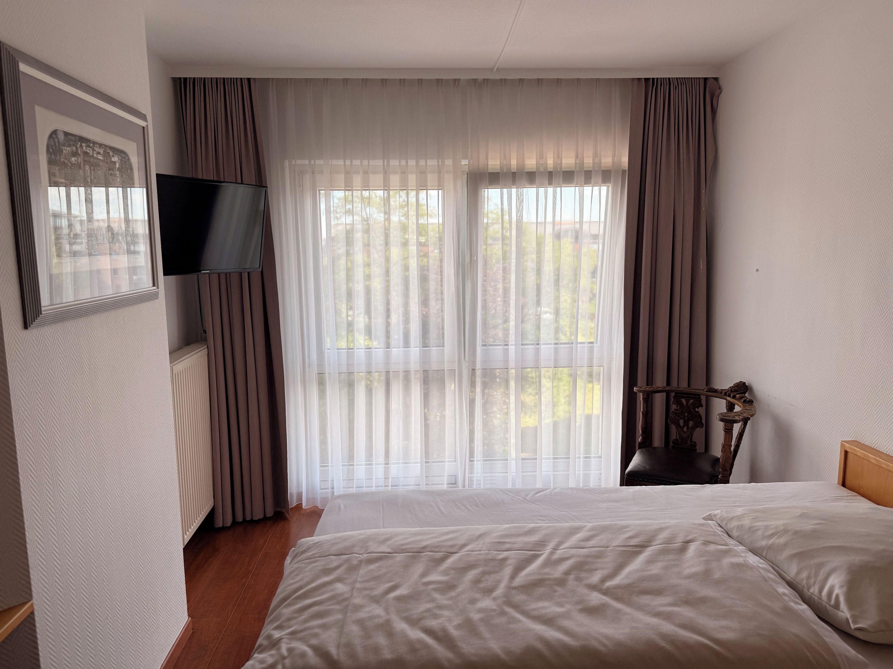 Una habitación de hotel con cama, televisión, silla y ventana con cortinas.