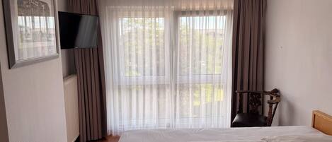Una habitación de hotel con cama, televisión, silla y ventana con cortinas.