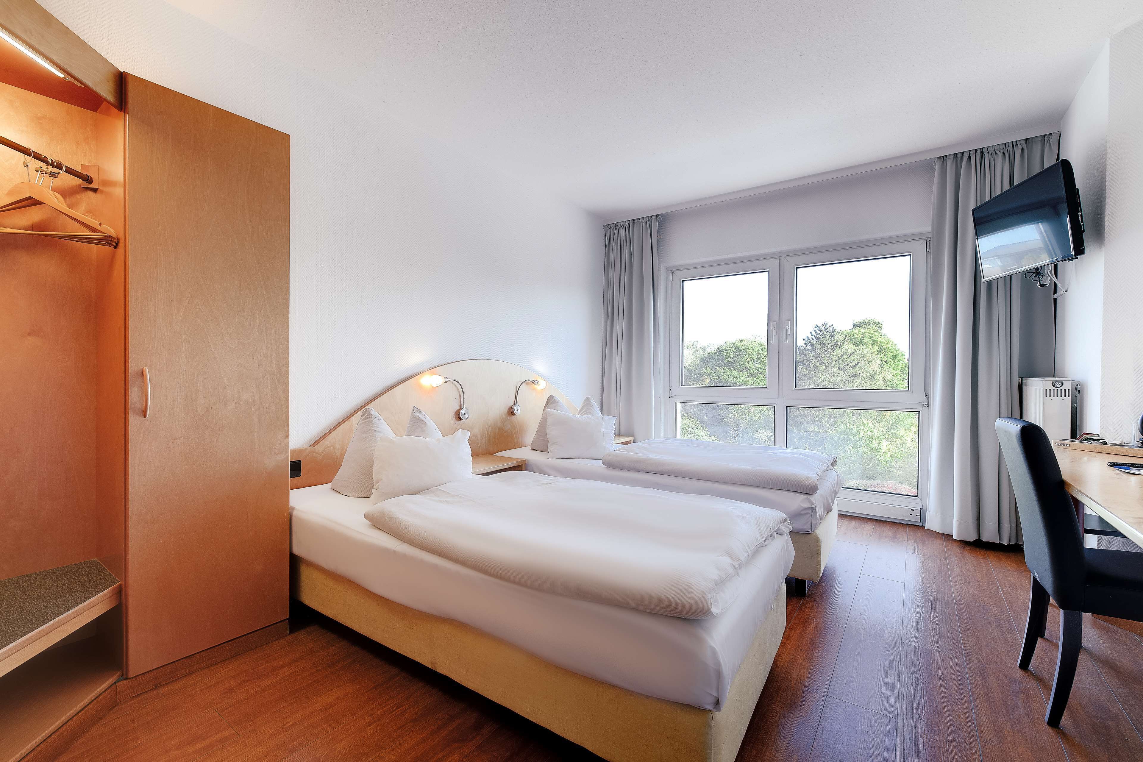 A hotel room with two beds, a desk, a TV, and a wardrobe.