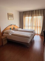Habitación de hotel con cama doble, mesita de noche, lámpara y ventana con cortinas.