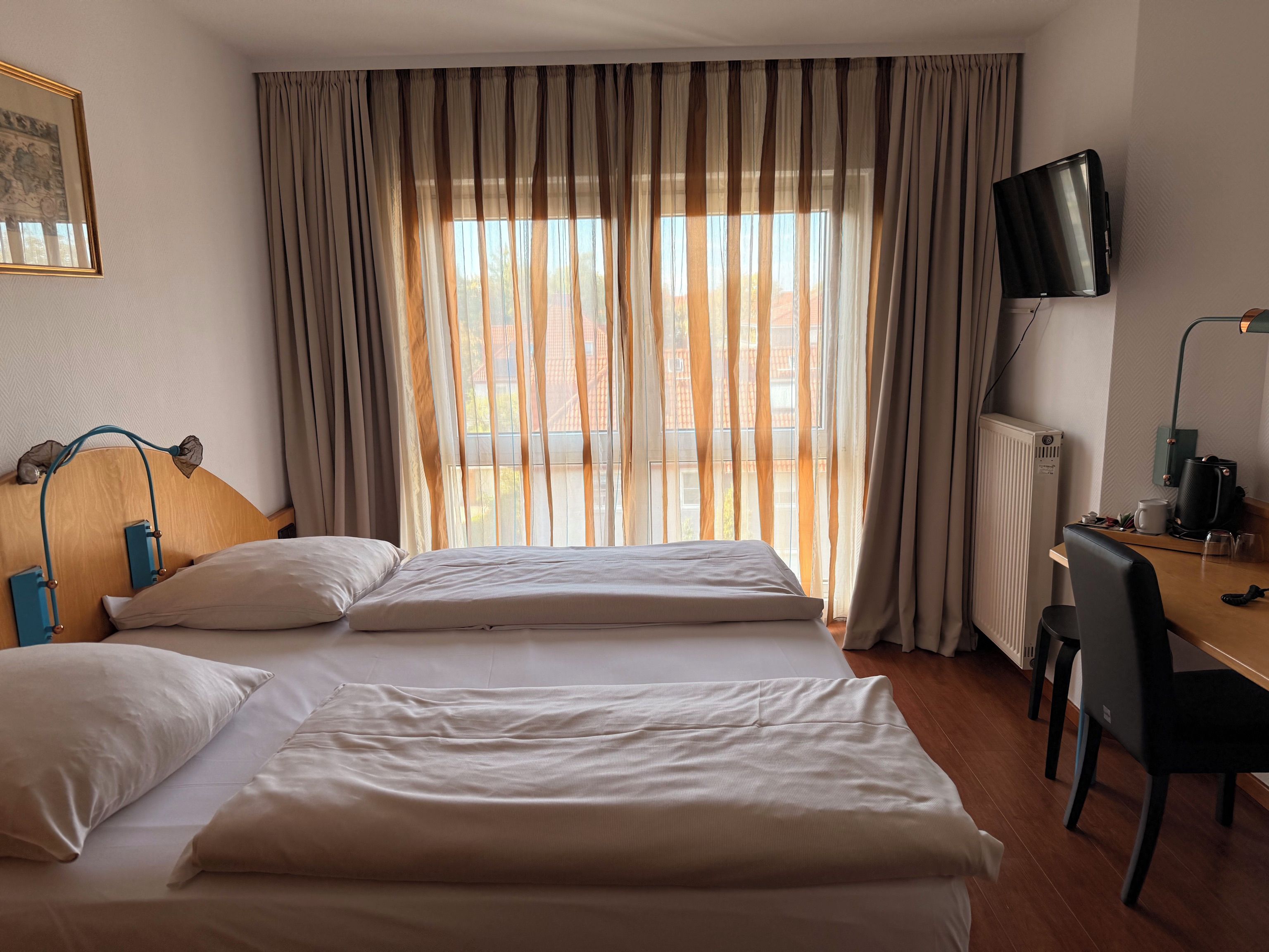 A hotel room with two beds, a desk with a chair, a television, and a window with curtains.