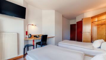 Habitación de hotel con dos camas, un escritorio con silla, televisor montado en la pared y armario con espejo.