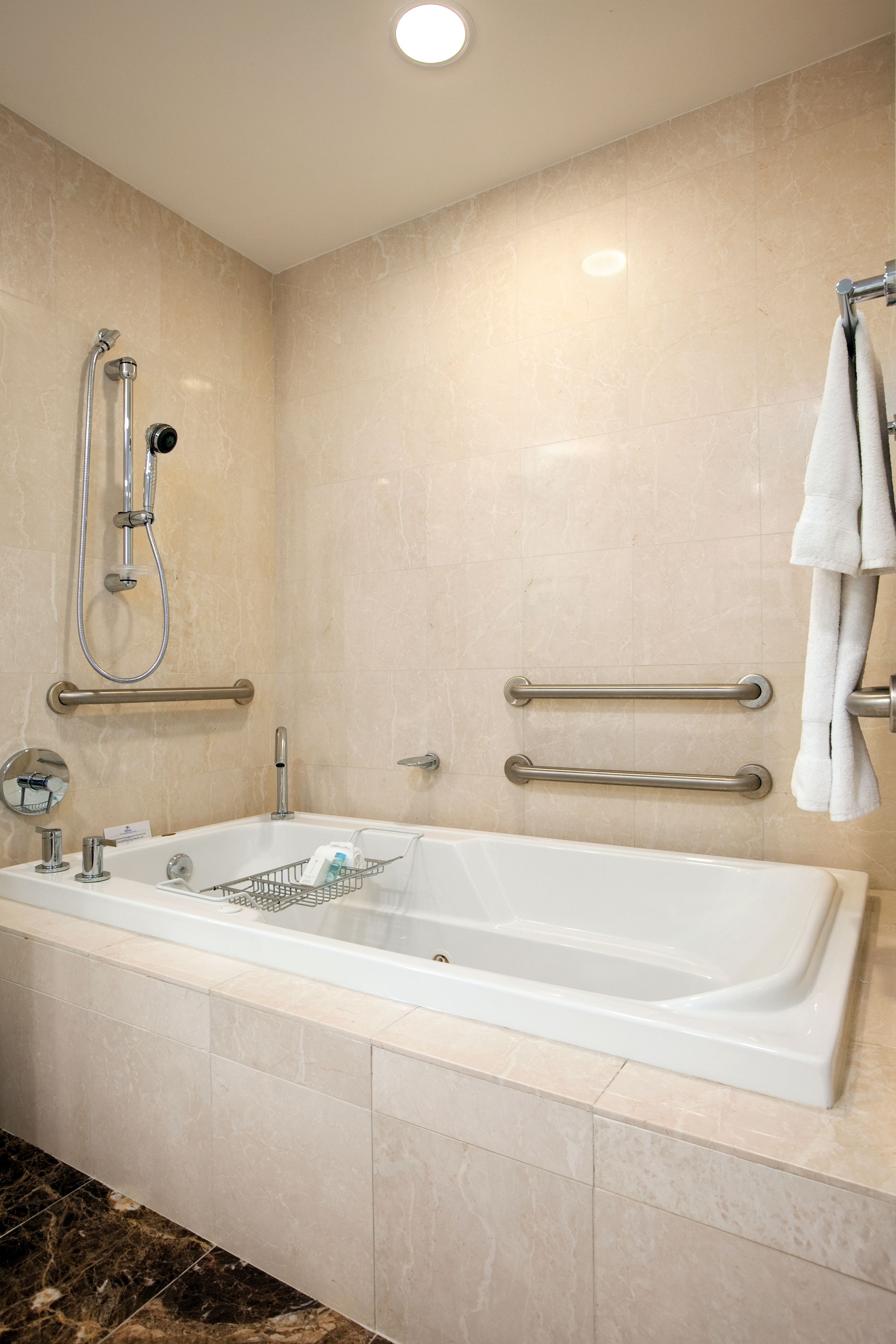A modern bathroom with a bathtub, grab bars, a showerhead, and a towel rack.