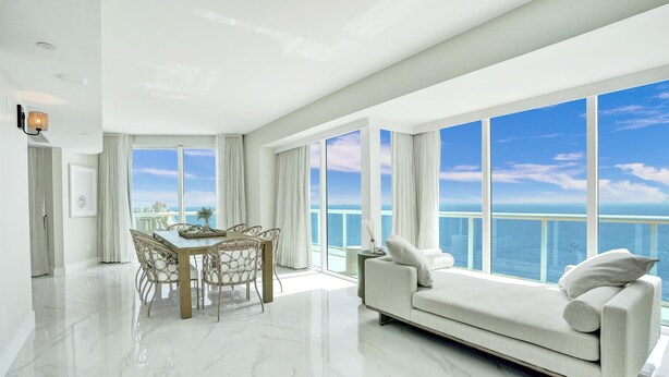 A spacious living room with a large window overlooking the sea, a modern dining area, and a plush sofa.