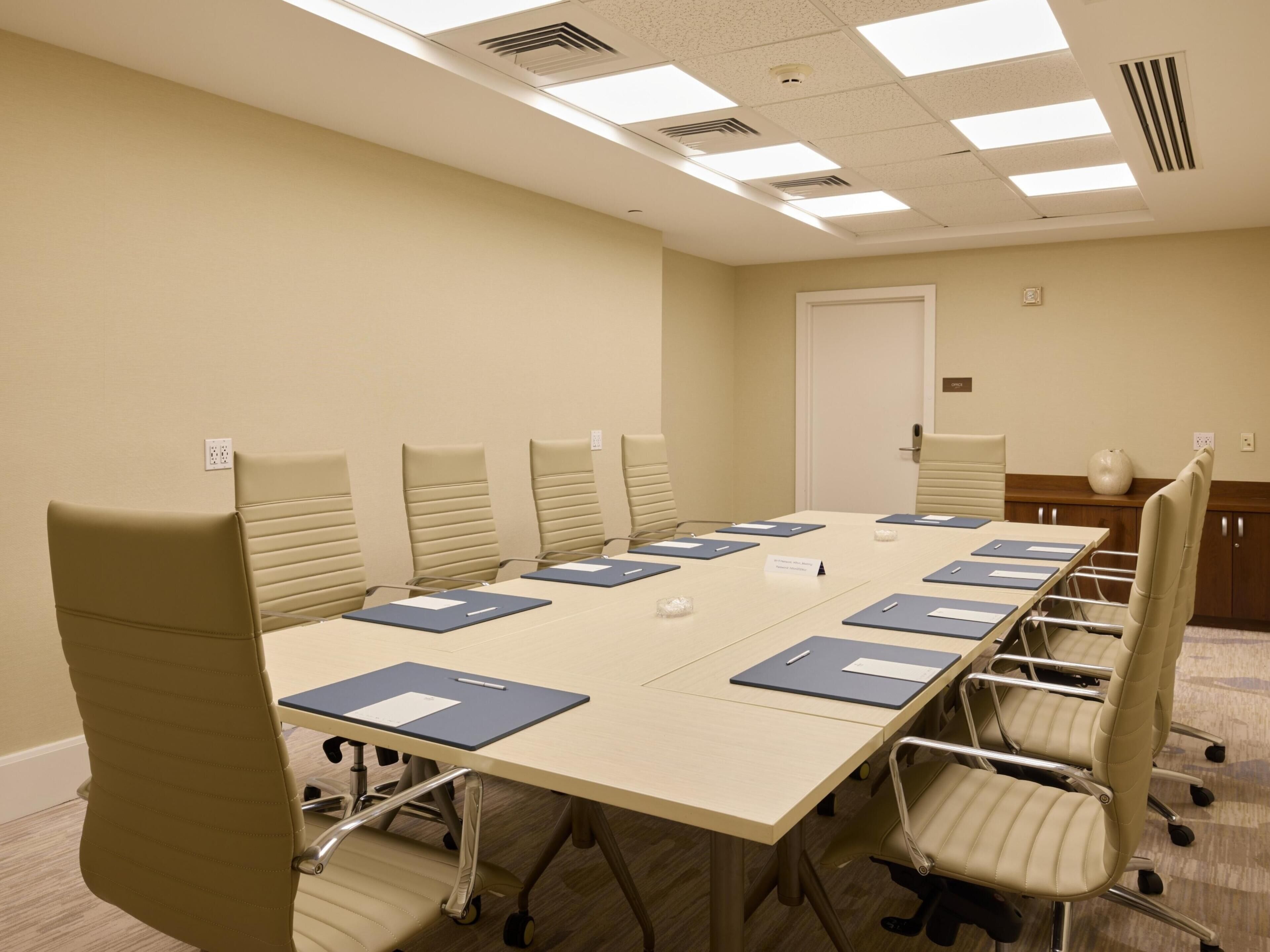 A conference room with a long table, multiple chairs, nameplates, and a door in the background.