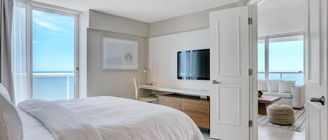 A modern bedroom with a bed, a desk, a TV, and a view of the sea.