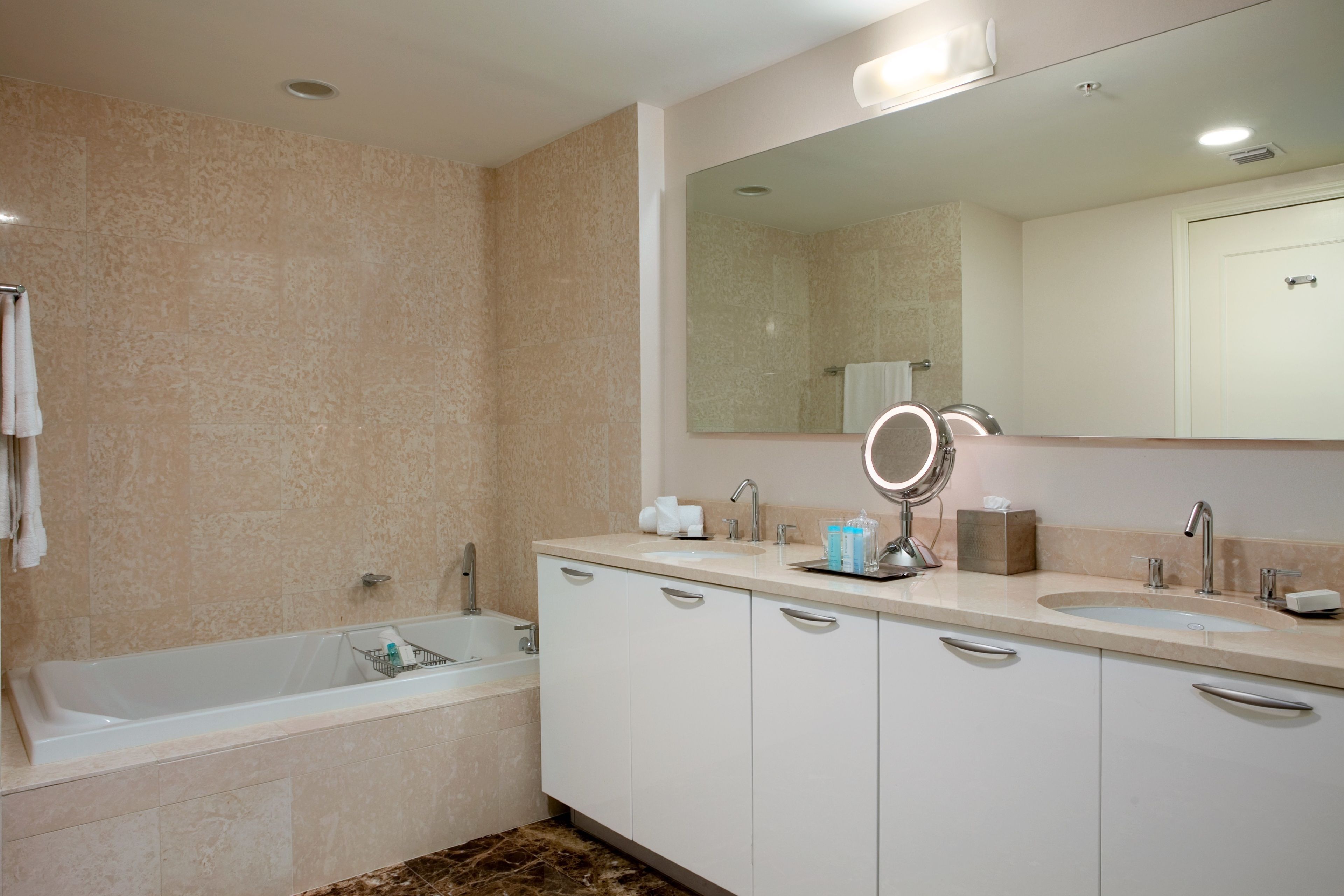 A modern bathroom with a bathtub, two sinks, and a large mirror.