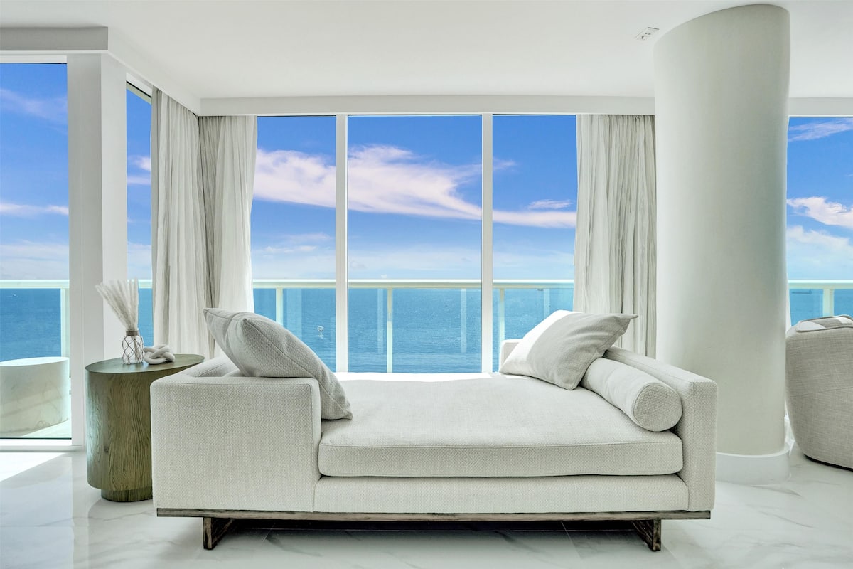 A modern living room with a large window overlooking a body of water, a white sofa, and a round side table.