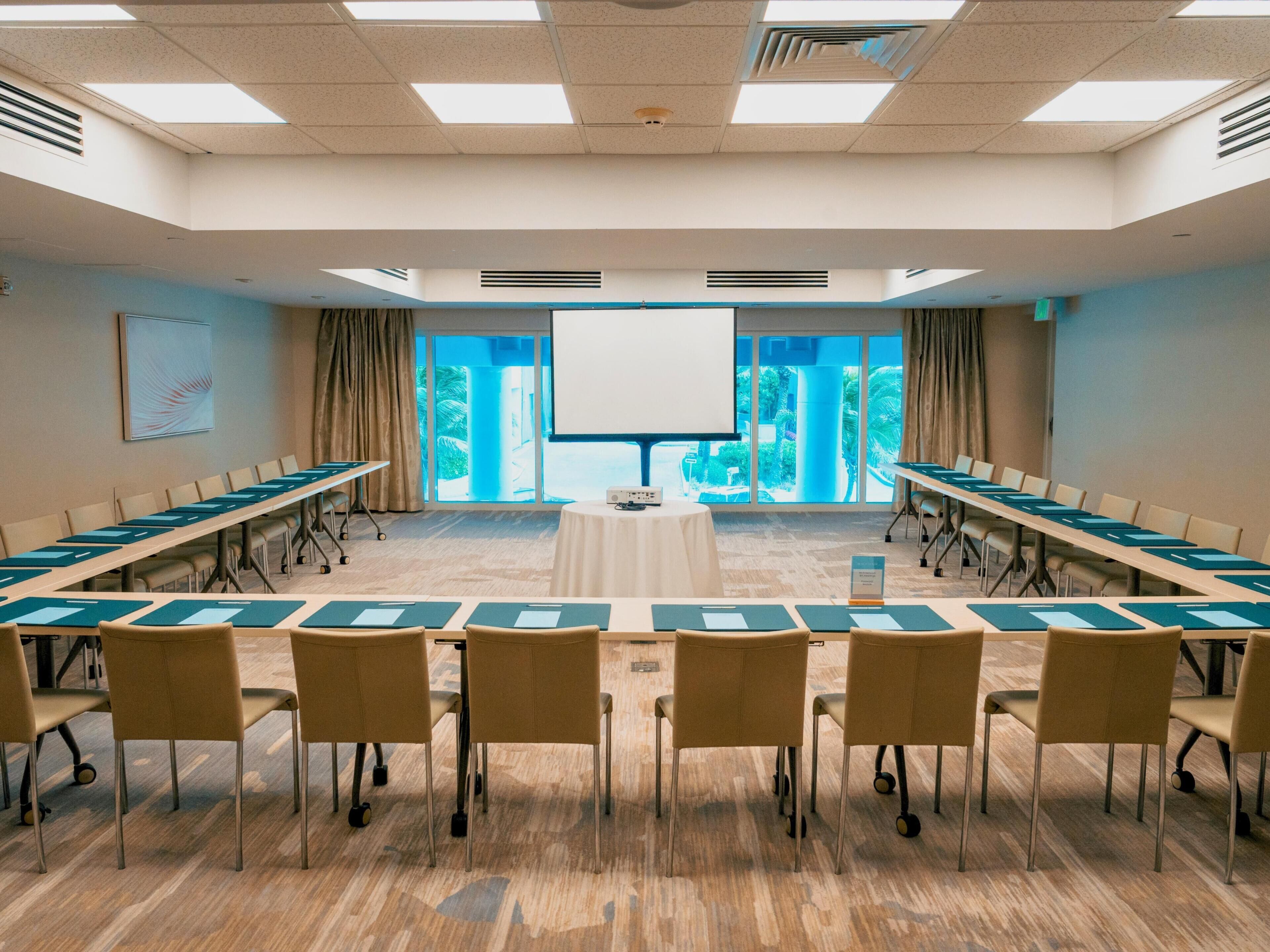 A conference room with a long table, chairs, a projector screen, and large windows.