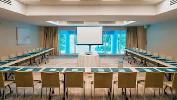 A conference room with a long table, chairs, a projector screen, and large windows.