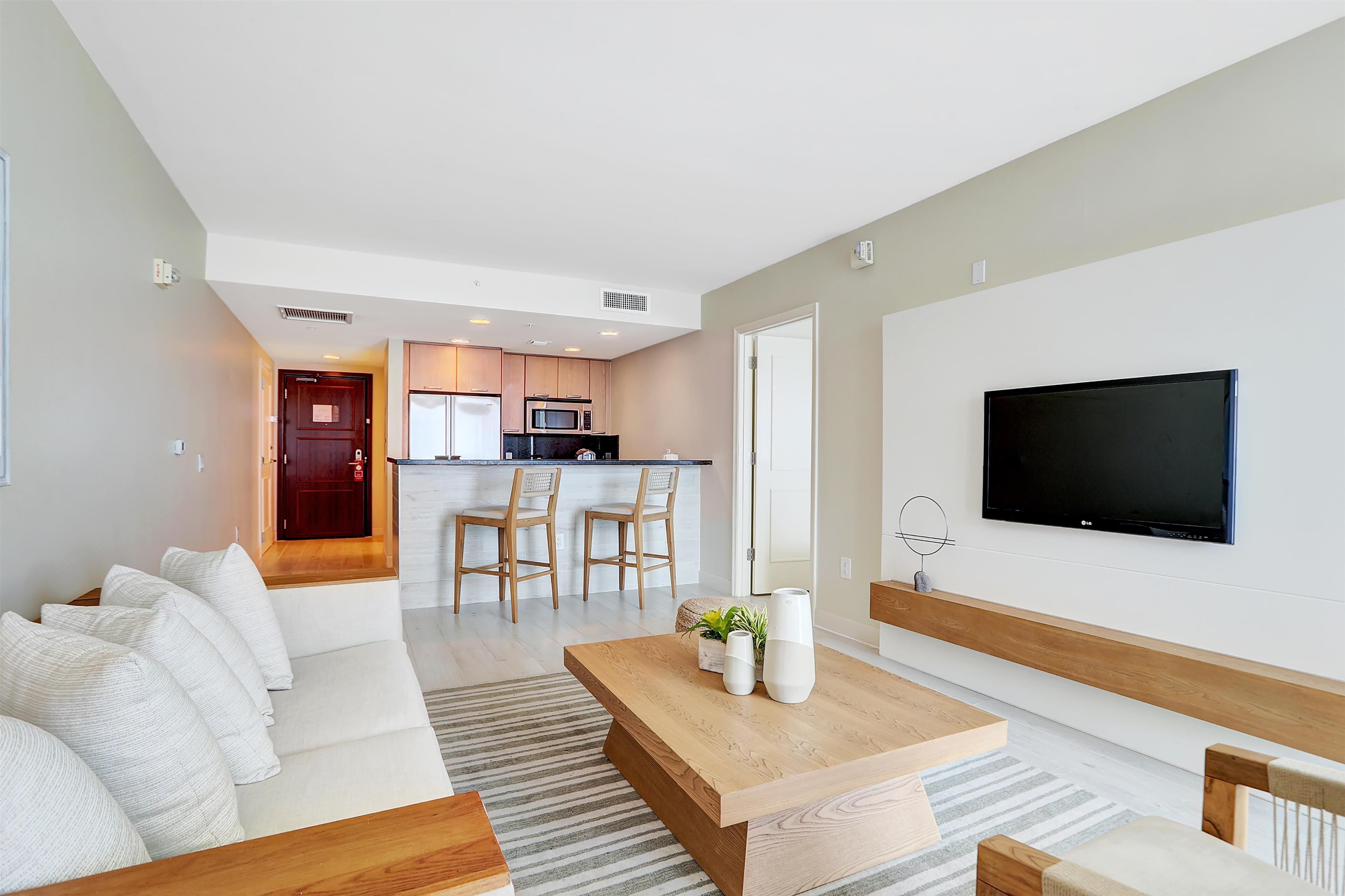 Una sala de estar moderna con una mesa de centro de madera, sofás blancos y un televisor montado en la pared.