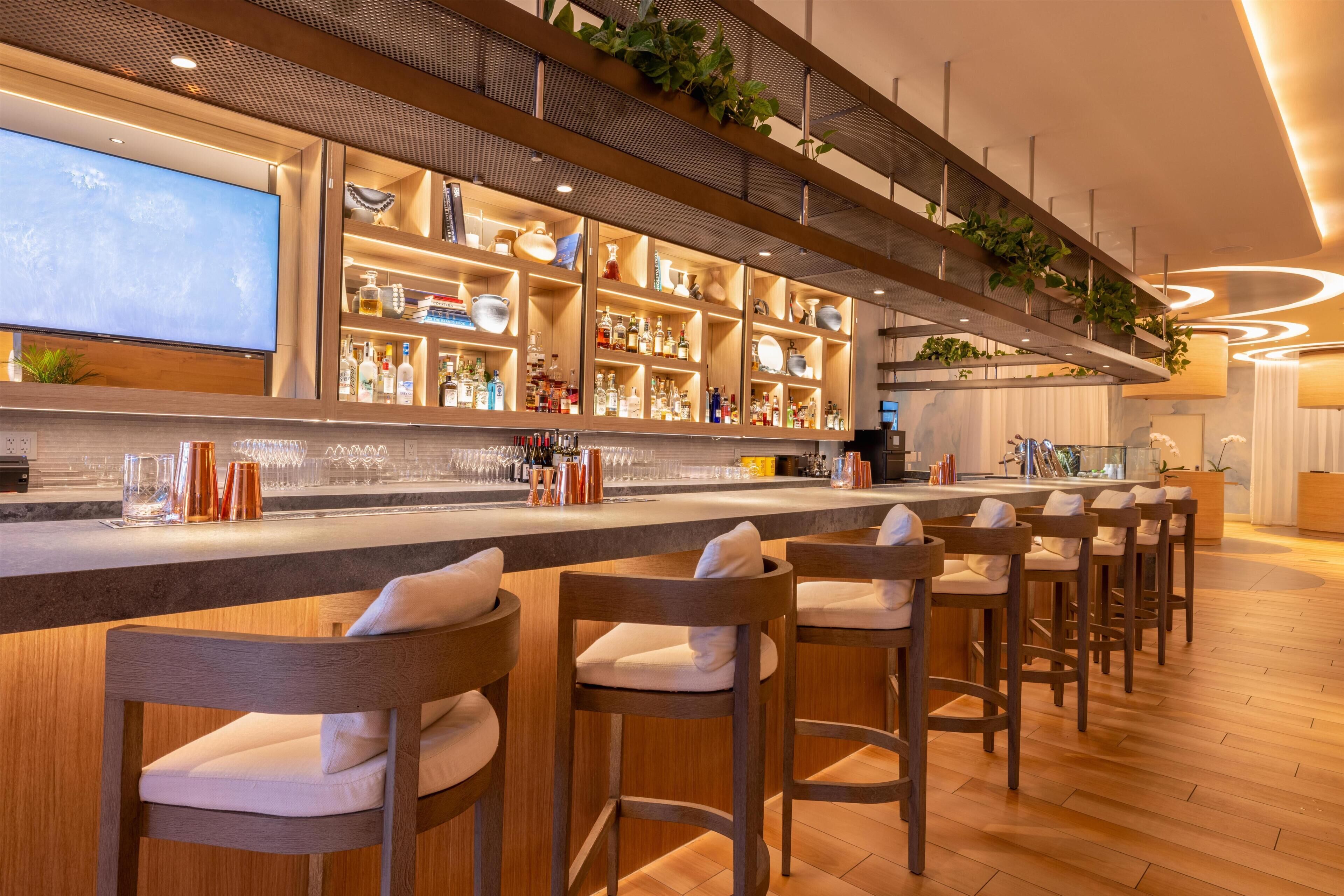 A bar area with a long counter, multiple shelves with bottles, and bar stools.