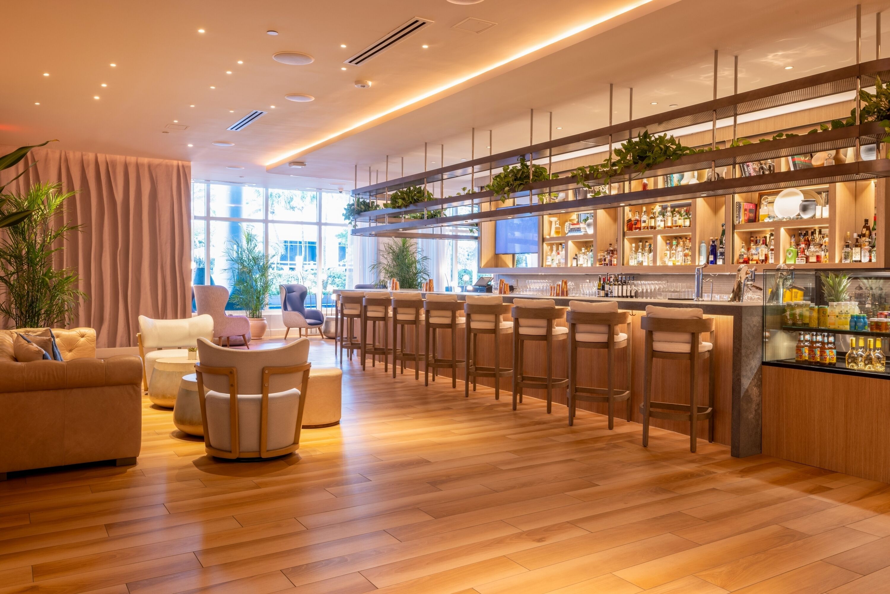 Zona de bar moderna con suelo de madera, taburetes y una variedad de botellas.