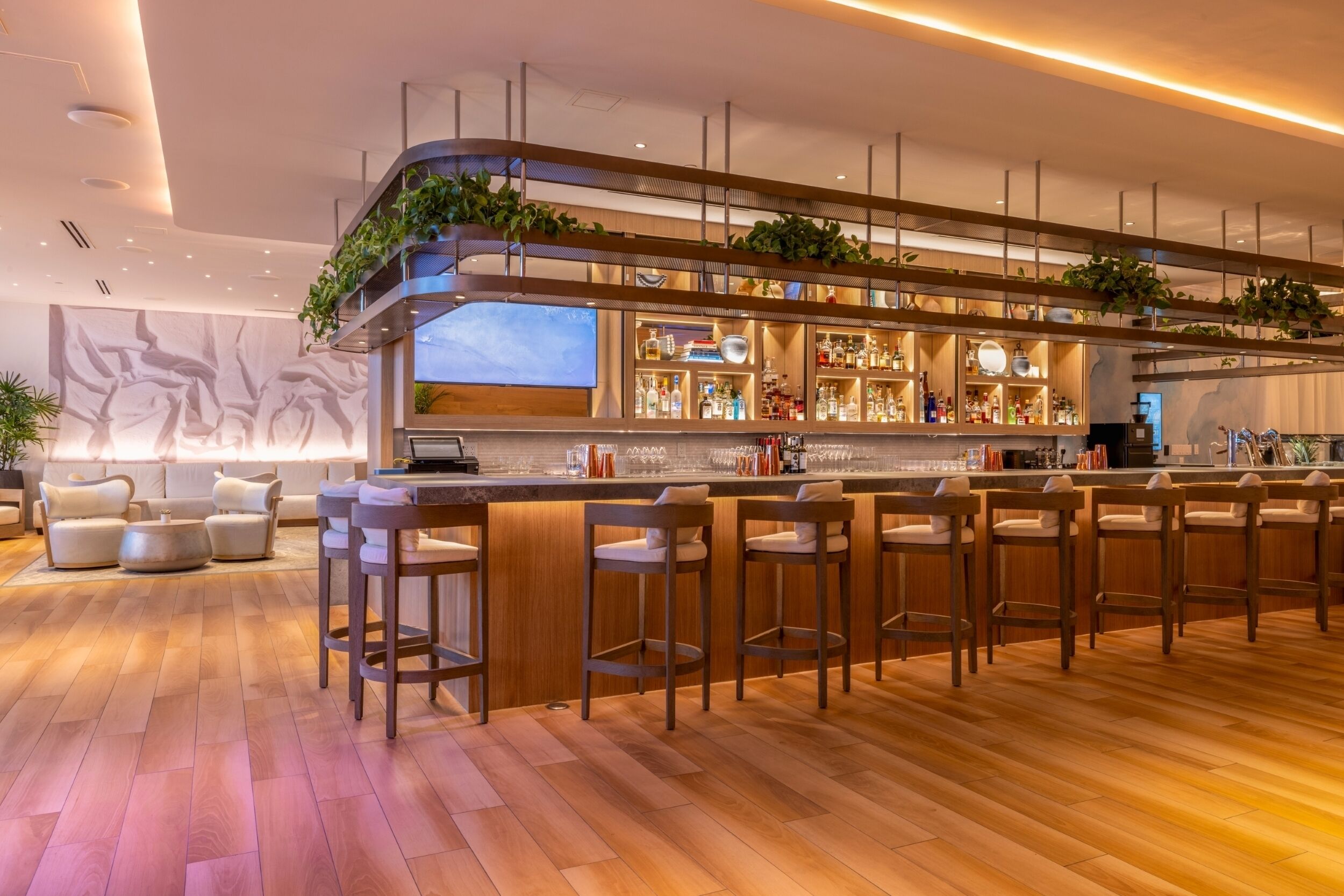 Un área de bar moderna con varios taburetes, una barra y estantes llenos de botellas.