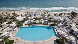 A resort with a central pool, beachside lounge areas, and a view of the ocean.