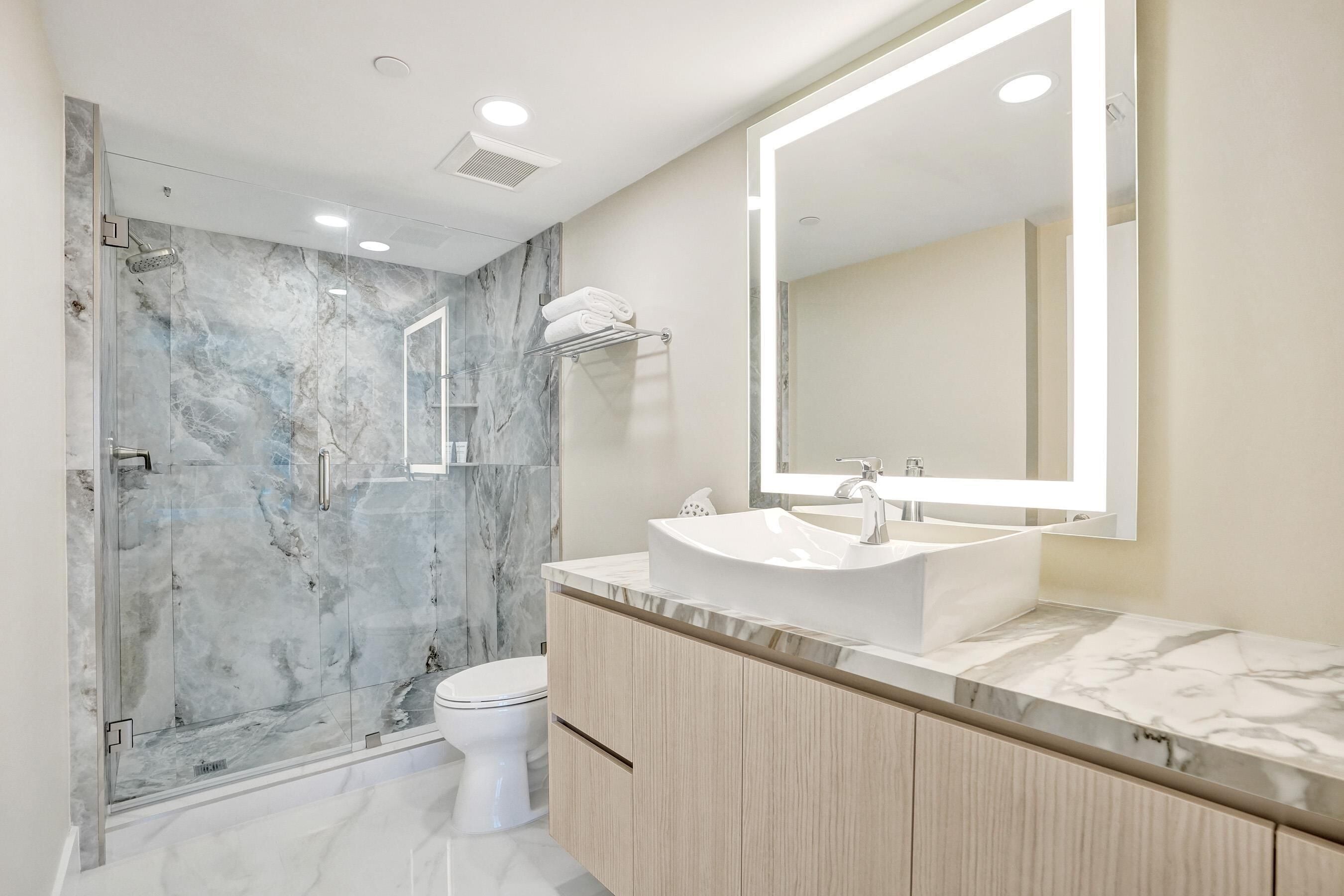 Een moderne badkamer met een marmeren douche, een witte wasbak en een grote spiegel.