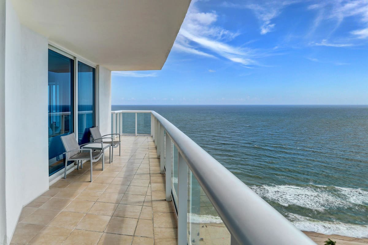 A balcony with a view of the ocean, a tiled floor, and a railing.