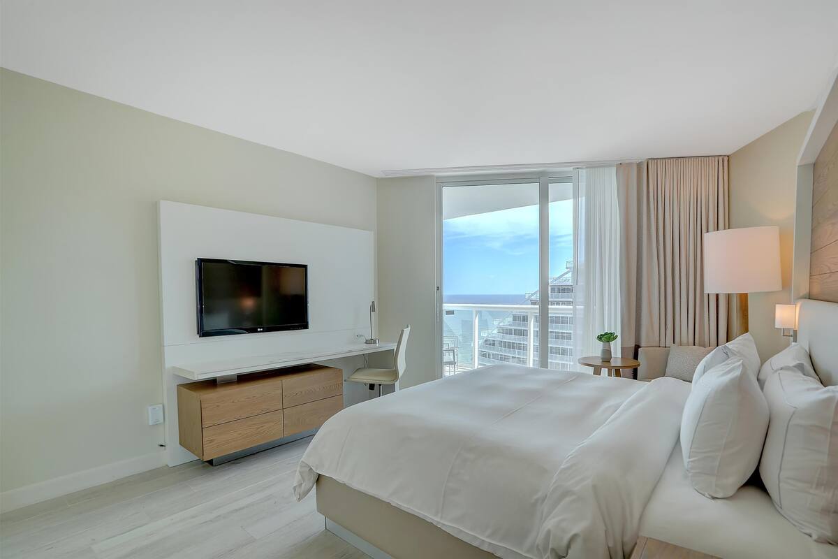 A modern hotel room with a large bed, a flat-screen TV, a desk, and a view of the city.