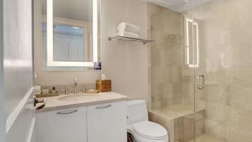 A modern bathroom with a glass-enclosed shower, a white toilet, and a vanity with a mirror.
