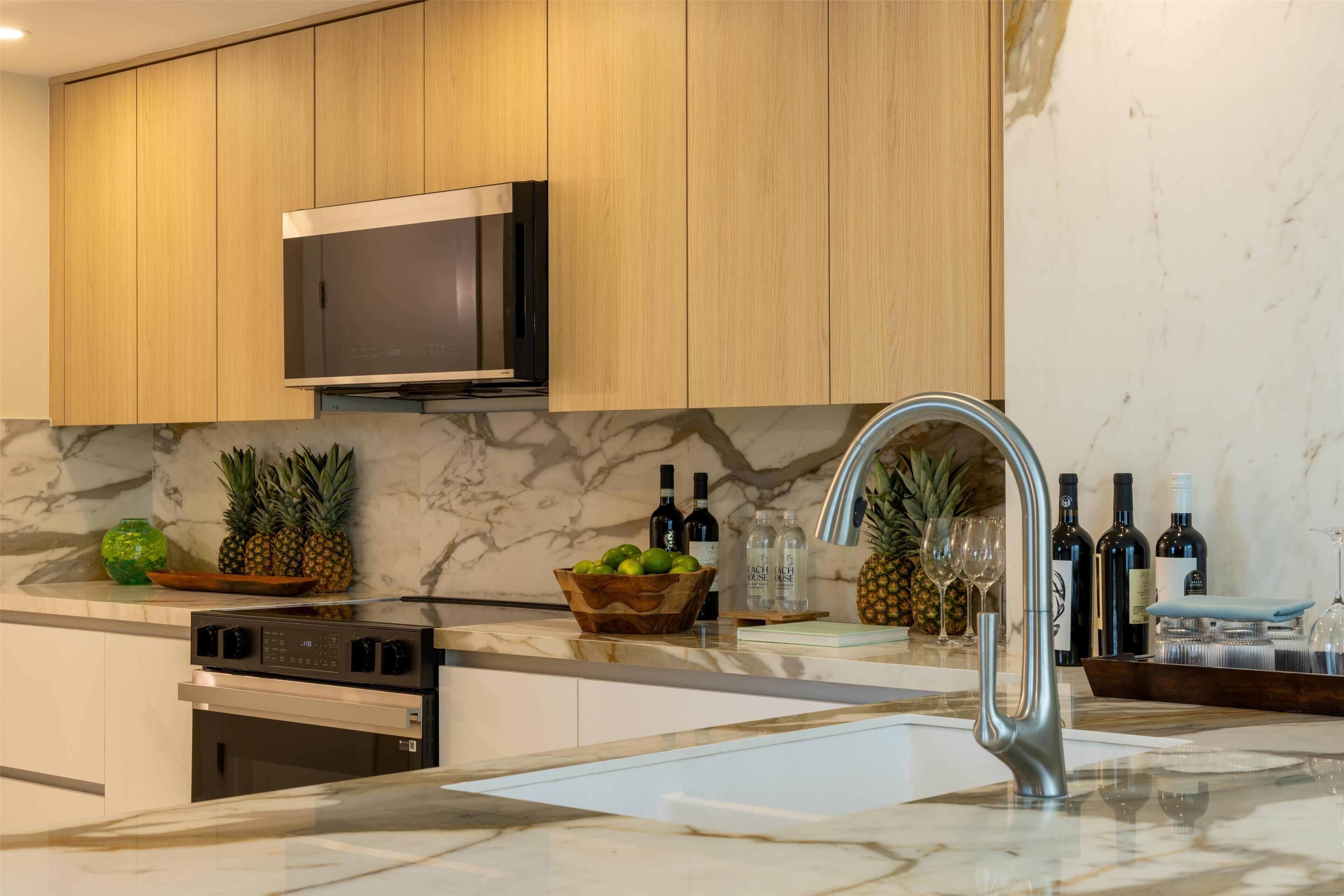 A modern kitchen with wooden cabinets, a stainless steel microwave, a built-in oven, a marble countertop, and a stainless steel sink.