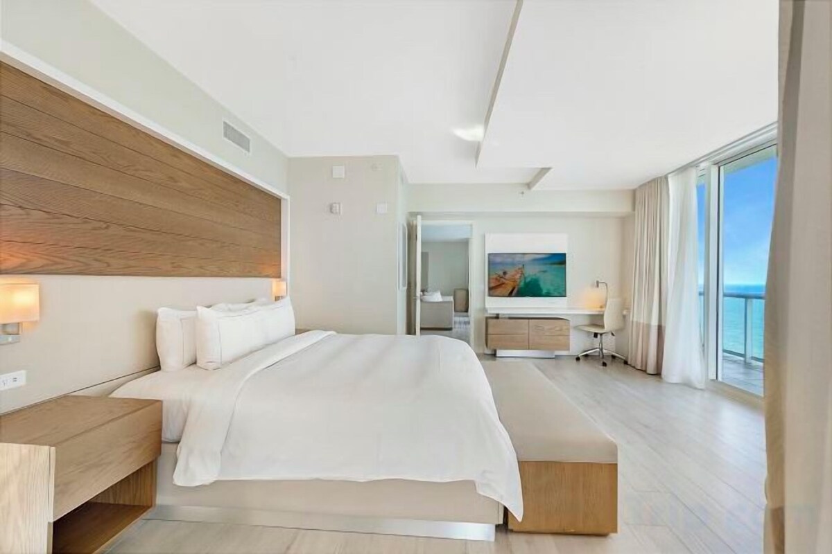 Une chambre d’hôtel moderne avec un grand lit, une tête de lit en bois et une vue sur la mer.