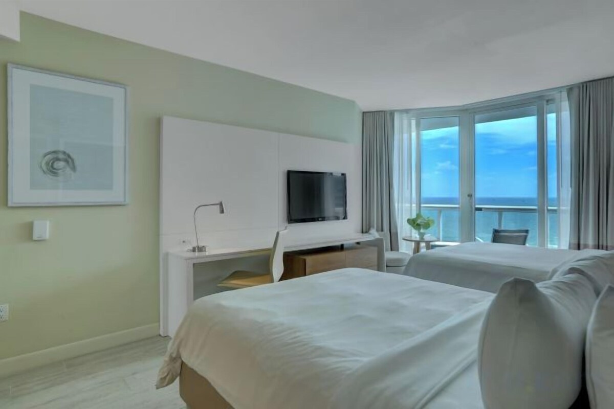 Une chambre d’hôtel avec un lit, un bureau avec une télévision et une vue sur la mer.