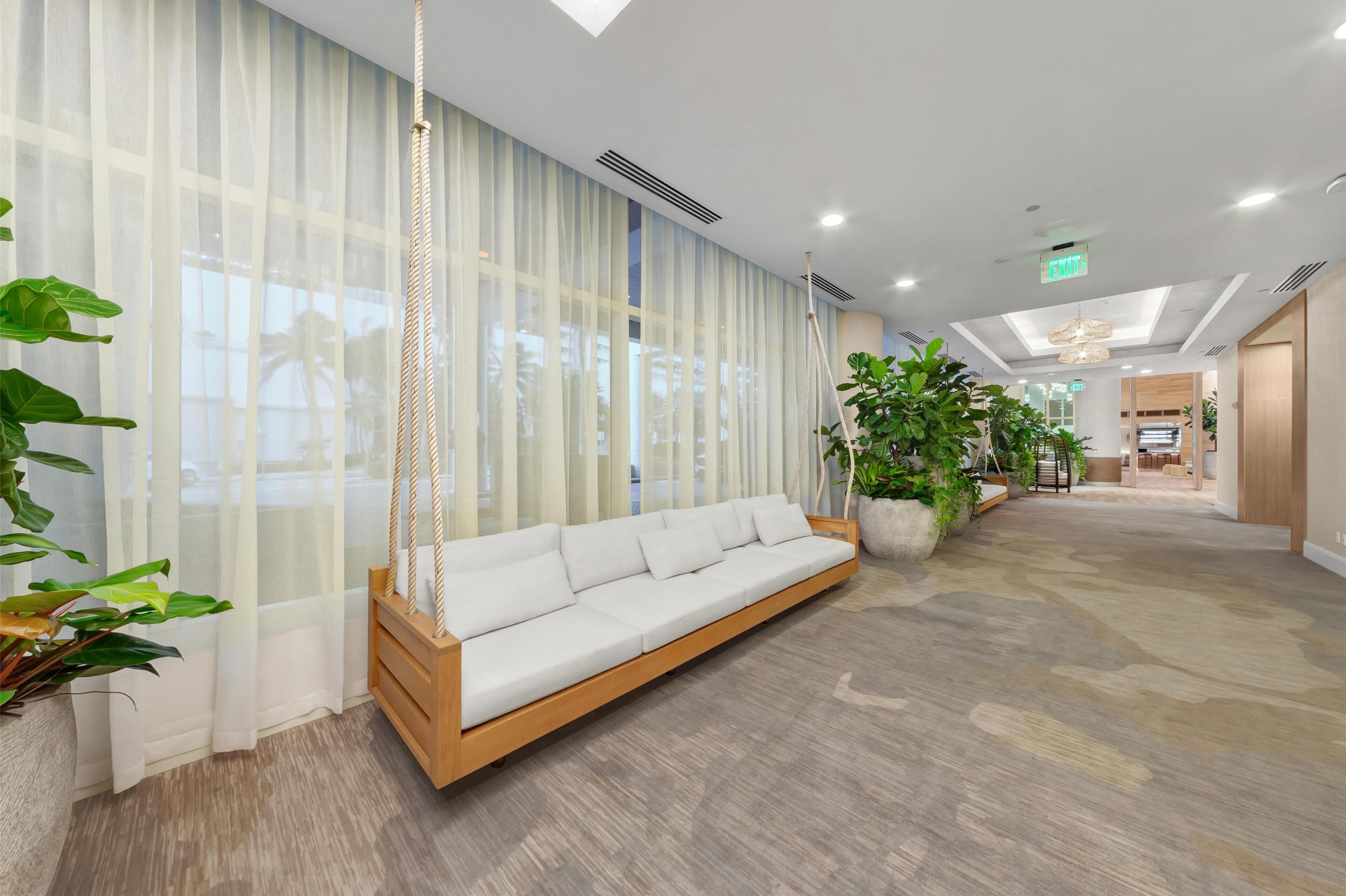Eine moderne Lobby mit einem weißen Sofa, großen Fenstern mit leichtem Vorhangstoff und Topfpflanzen.