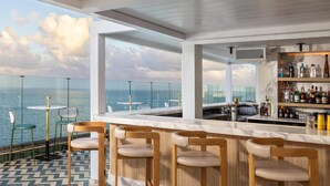 A bar area with a view of the sea, wooden bar stools, and a marble countertop.