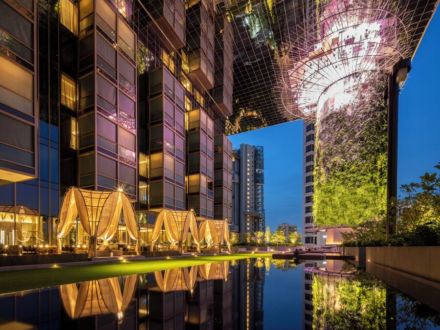 A modern building with reflective water in front, large windows, and a unique ceiling structure.