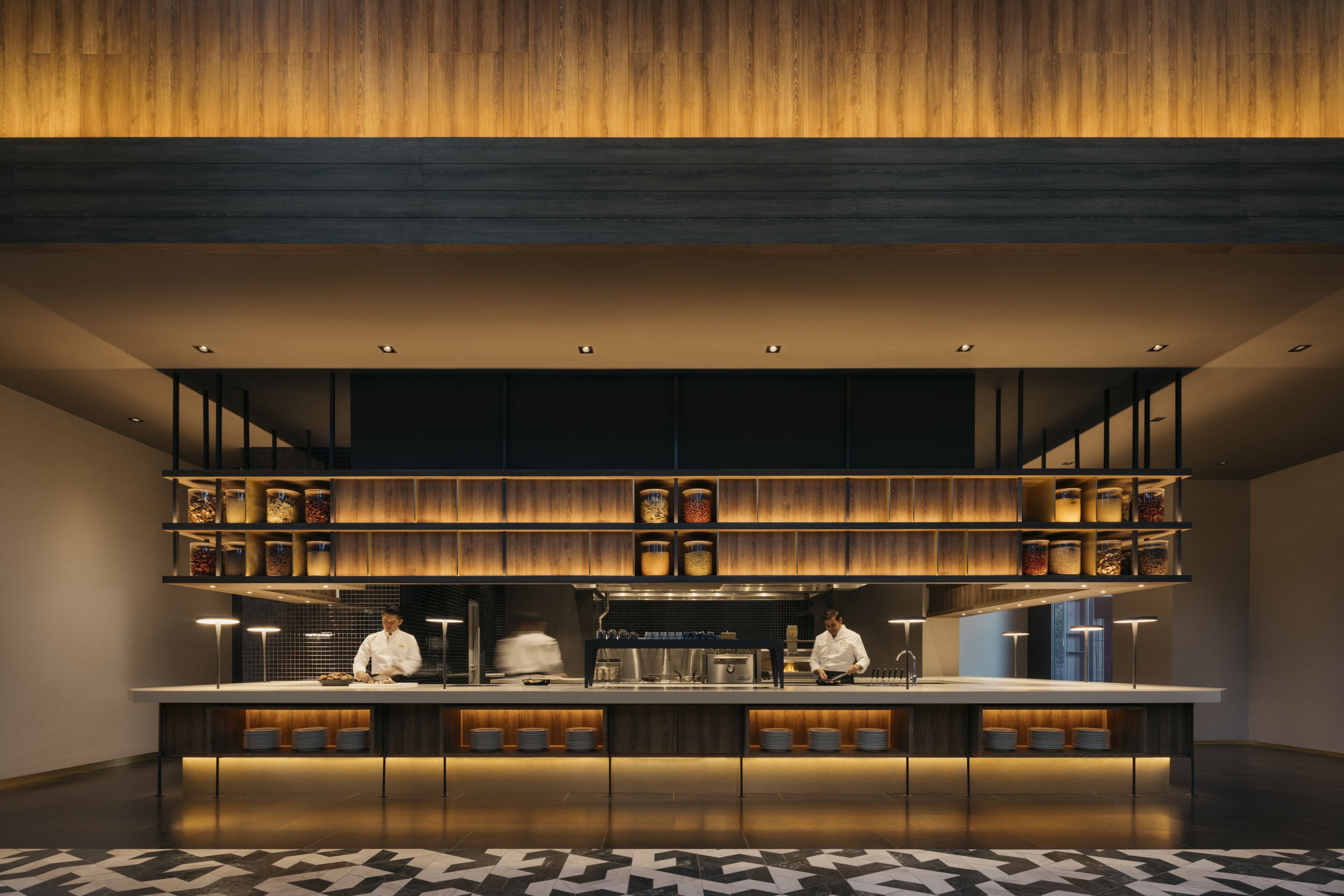 A modern kitchen with a central island, wooden shelves above, and a patterned floor.
