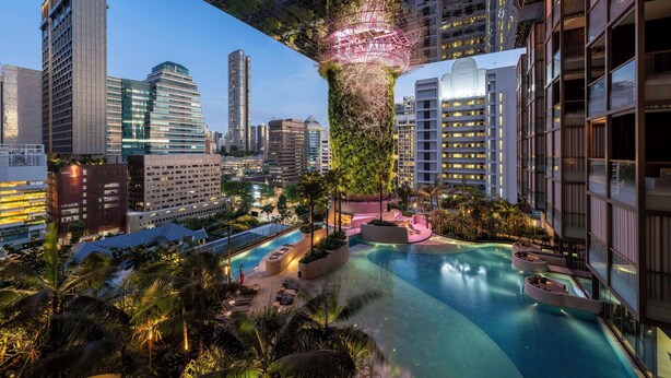 Um hotel moderno com piscina no terraço, vegetação exuberante e vista para a cidade.