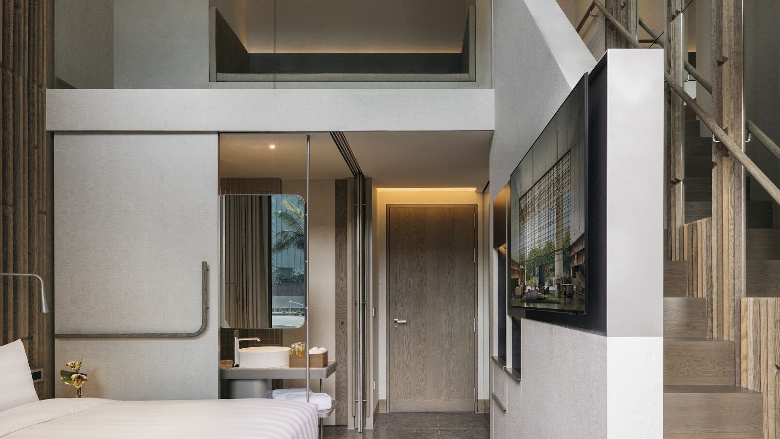 Una habitación de hotel moderna con cama, un baño con espejo grande y una escalera que lleva a un nivel superior.