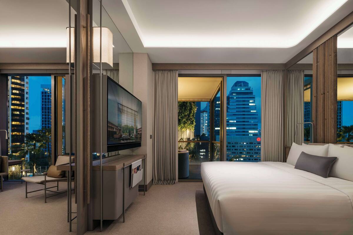 A modern hotel room with a large bed, a TV, and a balcony with a city view.