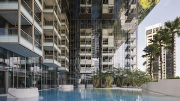 A modern building with a reflective glass facade, a central pool, and outdoor seating areas.