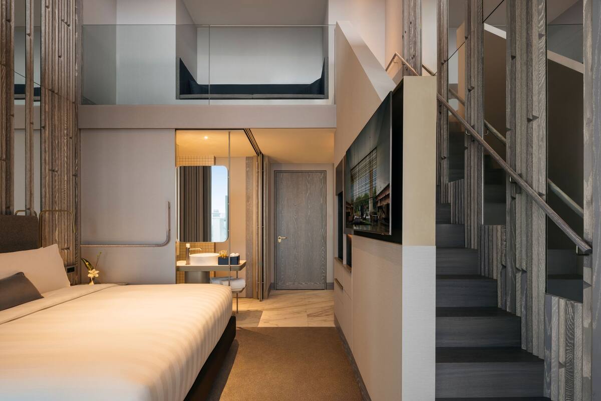 A modern hotel room with a bed, a small desk, a bathroom, and a staircase.