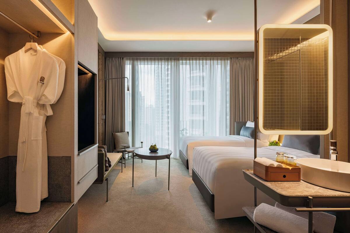 A hotel room with a bed, a desk with a mirror, a robe hanging, and a view of the city through large windows.