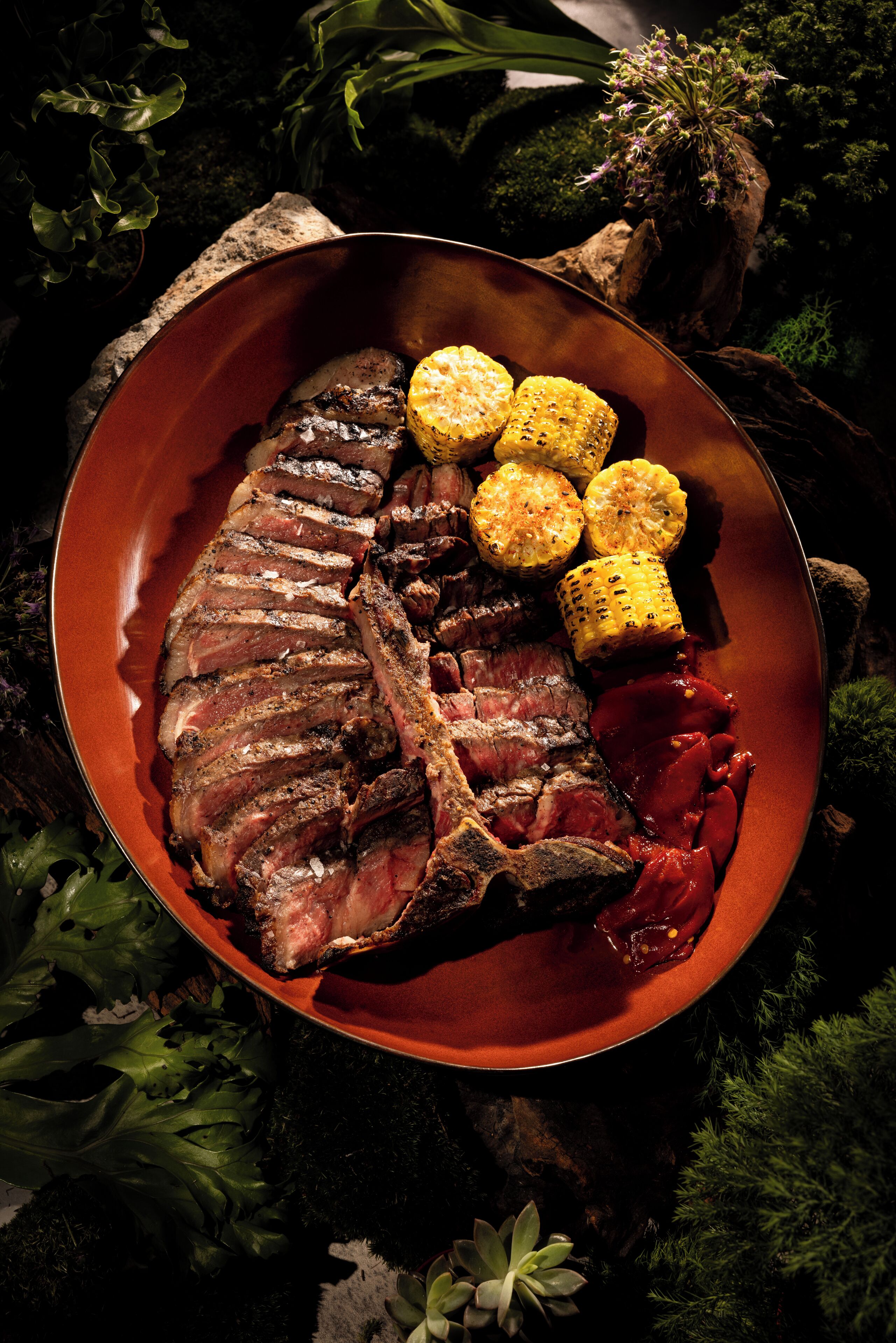 A plate of steak, corn on the cob, and a red sauce.