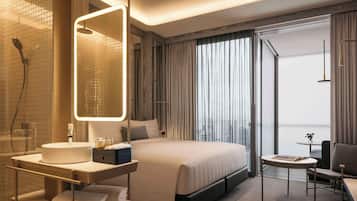A modern hotel room with a large bed, a bedside table with a lamp, a bathroom with a shower and sink, and a view of the city through the window.