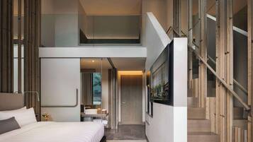 Een moderne hotelkamer met een groot bed, een badkamer met een spiegel, en een trap naar een hoger gelegen niveau.
