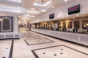 Eine Hotelhalle mit einer langen Rezeption, mehreren Sitzbereichen und einer Decke mit Oberlichtern.