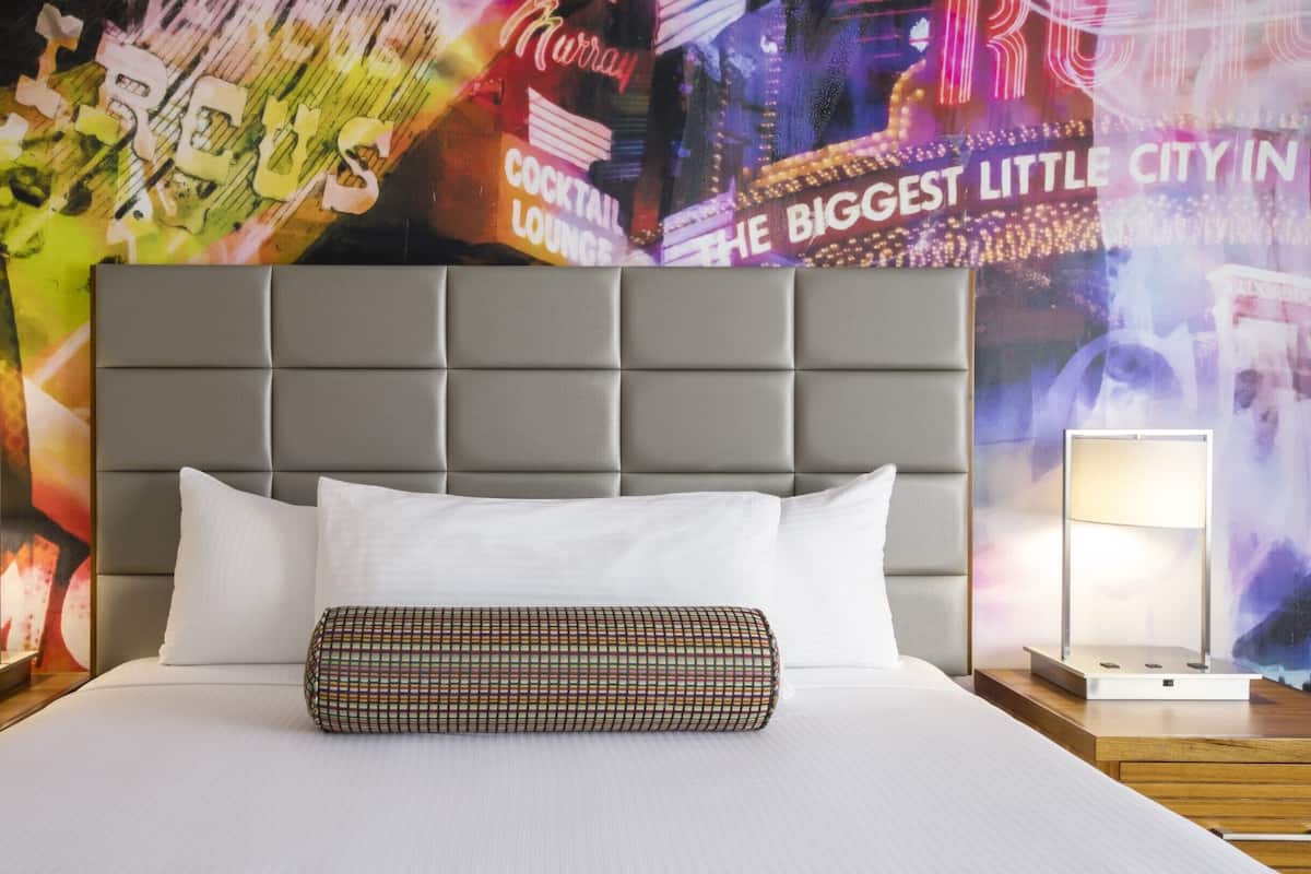 Ein Hotelzimmer mit einem großen Bett, einem grauen gepolsterten Kopfteil, weißer Bettwäsche und zwei Nachttischlampen.