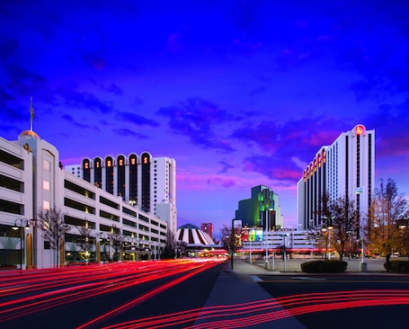 A city street at dusk with illuminated buildings and light trails from moving vehicles.