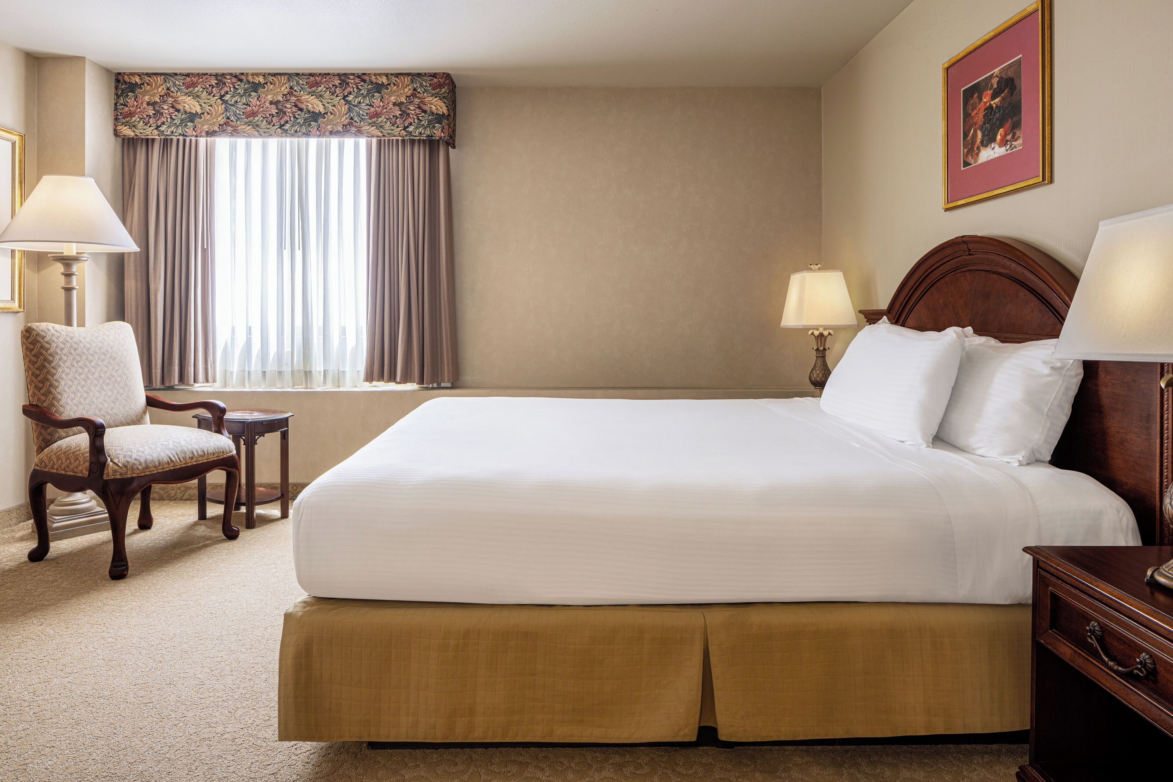 A hotel room with a large bed, a chair, a small table, and two lamps.