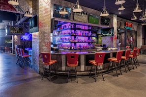 Un espace bar avec un comptoir, de nombreuses étagères remplies de bouteilles et des tabourets de bar rouges.