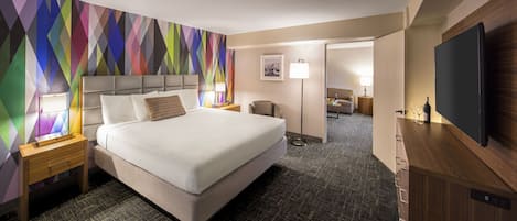 Ein Hotelzimmer mit einem großen Bett, einem Flachbildfernseher, einem Schreibtisch und einem farbenfrohen geometrischen Wanddesign.