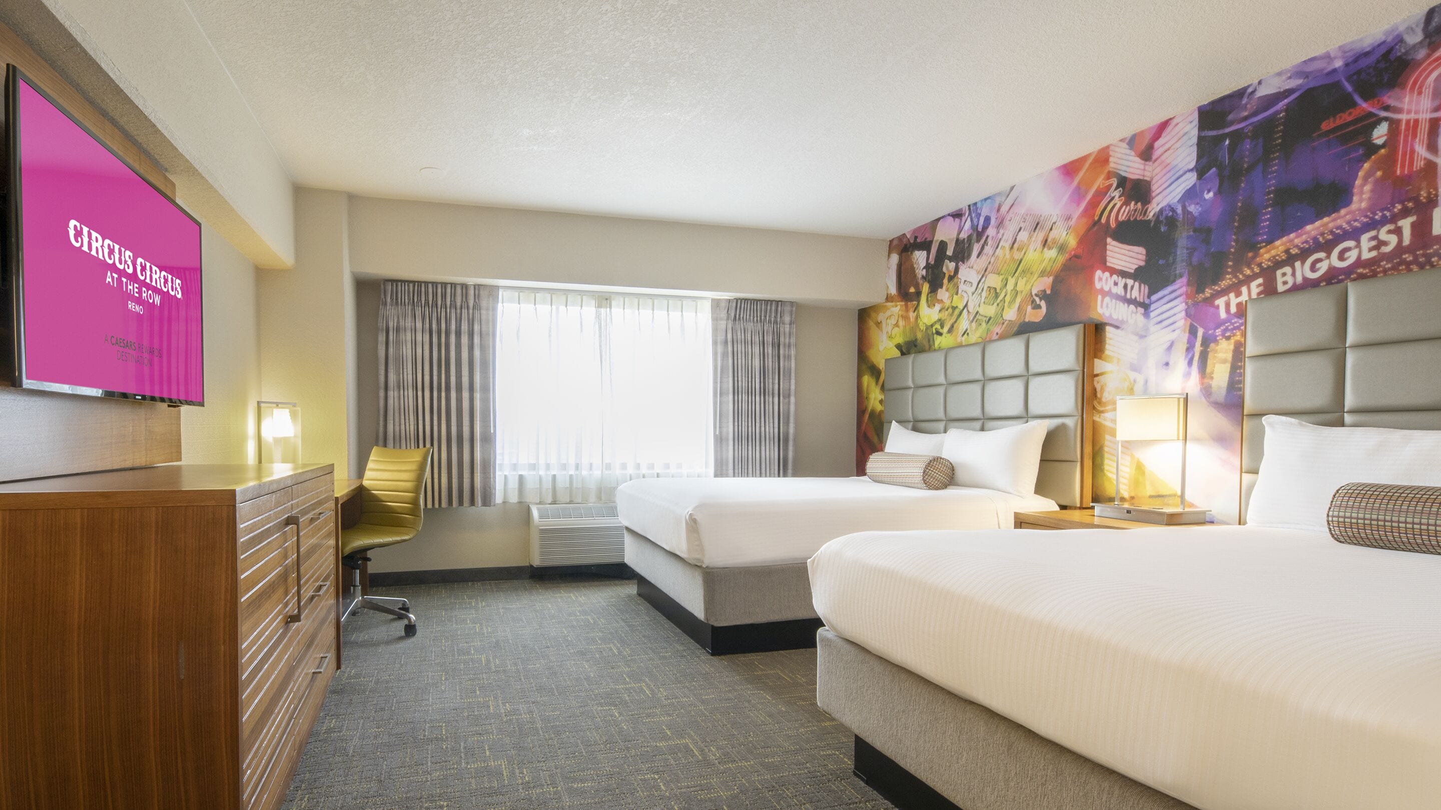 A hotel room with two beds, a desk, a chair, a television, and a large poster on the wall.