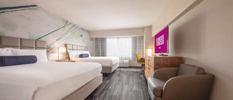 A hotel room with two beds, a desk, a chair, and a TV.