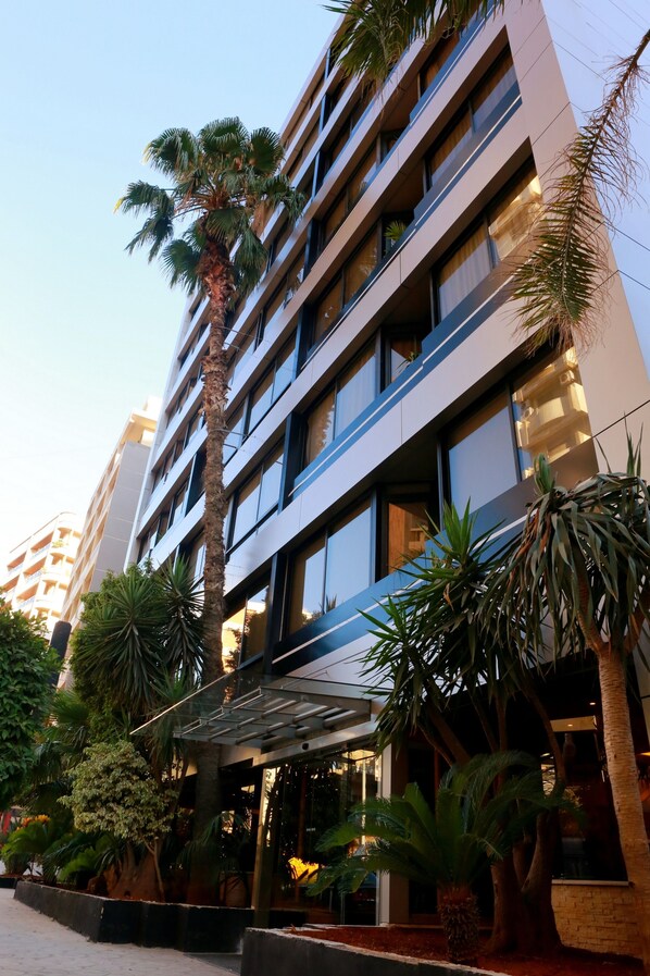 Un edificio moderno con varios pisos, ventanas amplias y un espacio al aire libre cubierto con plantas.