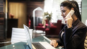 A person sitting at a glass table with a laptop, holding a phone to their ear. - Imperial Suites Hotel (Beirut)